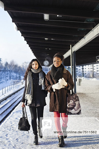 Young female friends in warm clothing walking on station platform