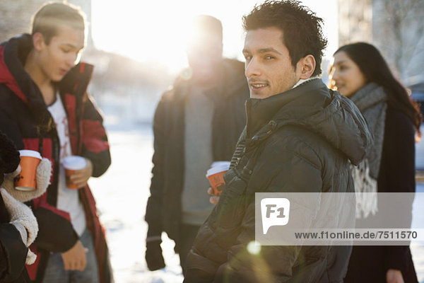 Portrait eines jungen Mannes mit Freunden in warmer Kleidung mit Einwegbechern