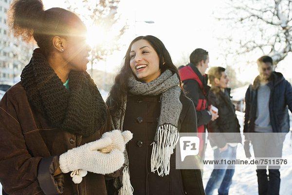 Glückliche junge Frauen in warmer Kleidung mit männlichen Freunden im Hintergrund