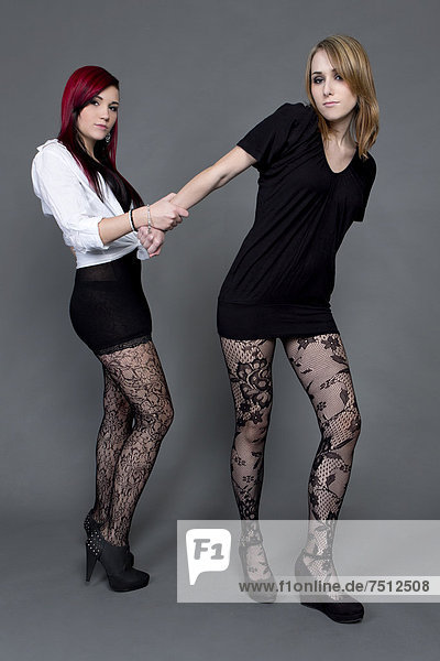 Zwei junge Frauen in kurzem Kleid  Strumpfhose und hohen Schuhen  halten sich
