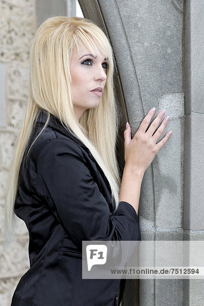 Junge Frau mit langen blonden Haaren und schwarzer Jacke posiert an Mauerbogen  Portrait