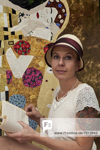 Woman with a tattoo wearing a Panama hat and reading a book in front of a patchwork of Klimt's The Kiss  Baden-Wuerttemberg  Germany  Europe