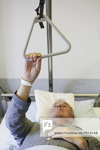 Senior in a hospital  holding a hand grip on a bed