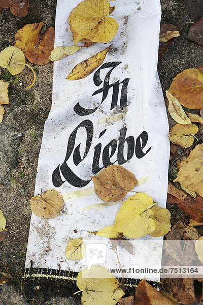 Ribbon with the message In Liebe  German for In Love  and autumn leaves on a grave