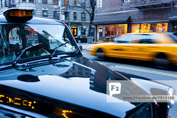 Ein typisches Taxi fährt durch New York  am Straßenrand parkt ein Londoner Taxi  New York City  Chelsea  USA