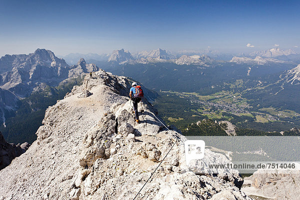 Climber walking on the Marino Bianchi fixed rope route  on Monte Cristallo mountain  on the way to the summit of Cristallo di Mezzo mountain  Monte Pelmo mountain at the back  the village of Cortina below  Belluno  Dolomites  Italy  Europe