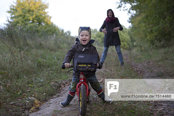 Ein kleiner Junge fährt lachend auf seinem Fahrrad einen Waldweg hinunter  Brandenburg  Deutschland  Europa