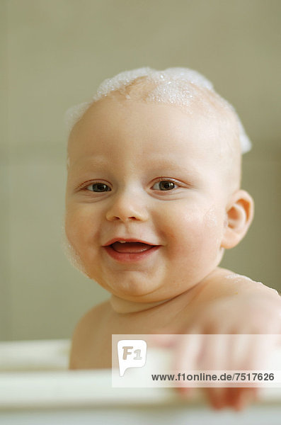 Baby in Badewanne  mit Schaum auf dem Kopf