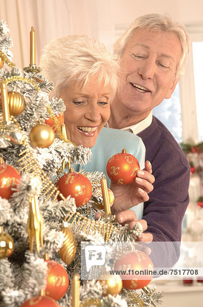 Älteres Paar schmückt lächelnd Weihnachtsbaum