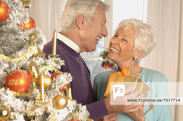 Mature couple with present next to a Christmas tree
