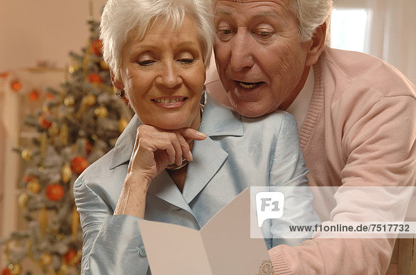 Mature couple reading Christmas cards in front of a Christmas tree