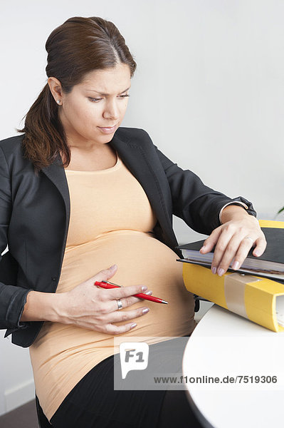 Schwangere Frau sitzt in einem Büro  besorgt