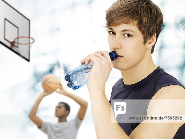 Young man  caucasian  holding a water bottle  in front of a young African American man with a basketball in a sports hall