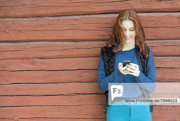 Young woman with red hair smiling and looking at her mobile phone