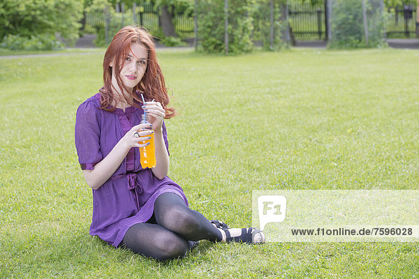 Young woman sitting in a park with a bottle of orange soda
