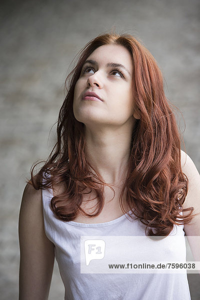 Pensive young woman with red hair looking up