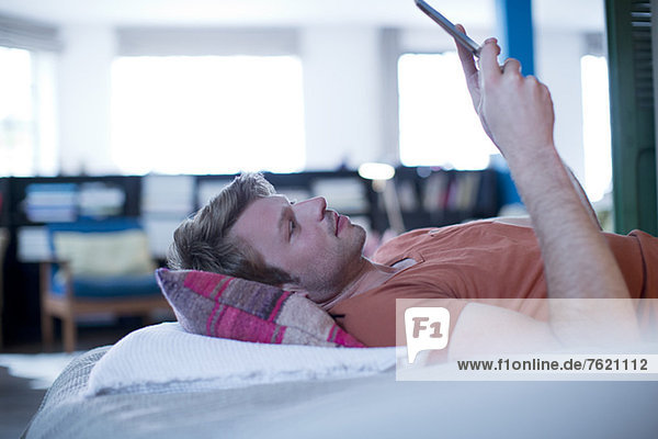 Mann mit digitalem Tablett auf dem Bett