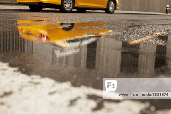 Taxi reflected in puddle on city street