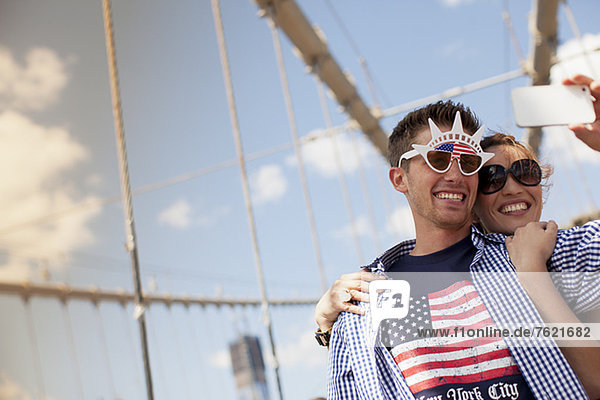Couple in novelty sunglasses taking picture on urban bridge