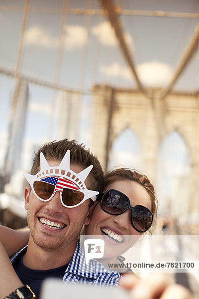 Couple in novelty sunglasses taking picture on urban bridge