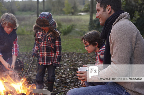 Vater und Kinder sitzen am Lagerfeuer