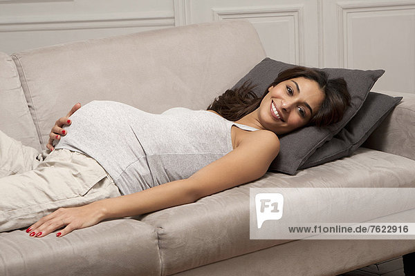 Schwangere Frau hält Bauch auf Sofa