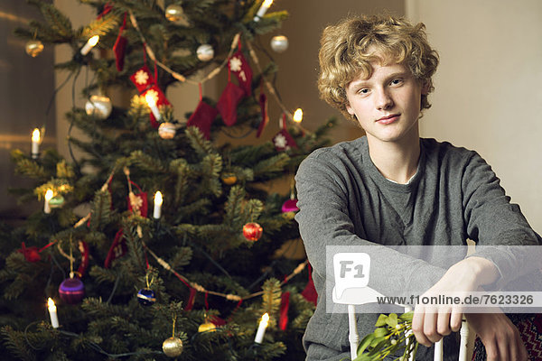 Teenager-Junge am Weihnachtsbaum sitzend