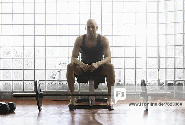 Mann sitzend mit Gewichten im Fitnessstudio