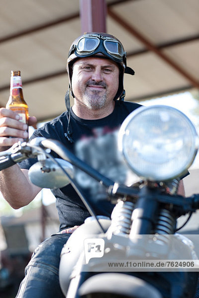 Mann trinkt Bier auf dem Motorrad
