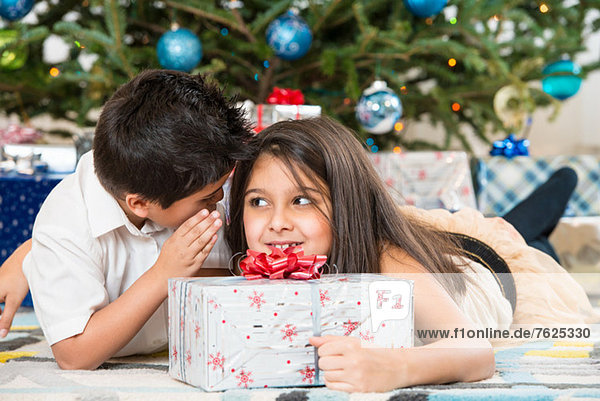 Children whispering by Christmas tree