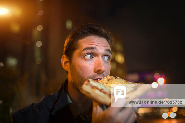 Mann isst Pizza auf der Stadtstraße