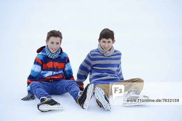 Zwei Jungen mit Schlittschuhen sitzen auf einem gefrorenen See