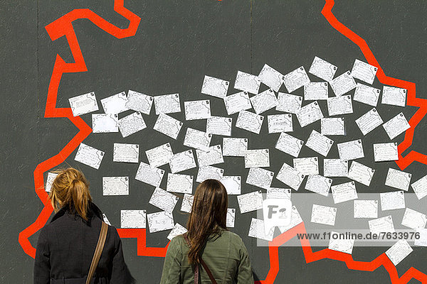 Zwei jugendliche Touristinnen stehen vor einer Mauer mit Postkarten die anläßlich der 775-Jahr Feier-Berlins am alten Schlossplatz in Berlin Mitte aufgestellt war  Berlin  Deutschland  Europa