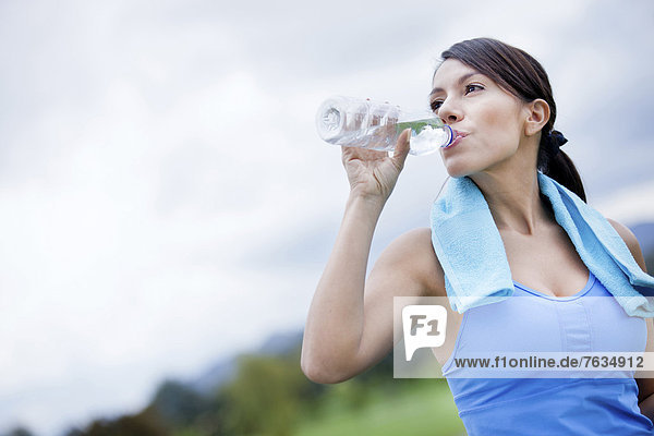 Frau in Sportkleidung trinkt aus Trinkflasche