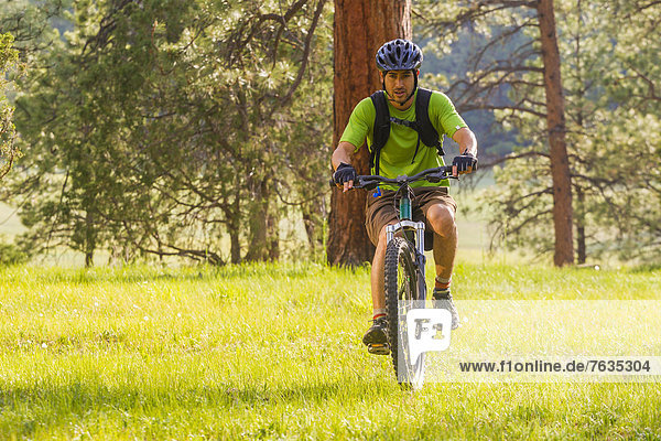 Hispanic man riding mountain bike in meadow