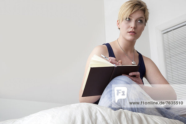 Caucasian woman writing in diary on bed