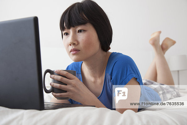 Chinese woman using laptop on bed