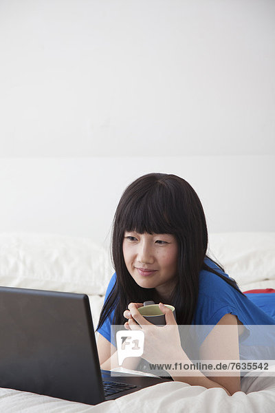 Chinese woman using laptop on bed