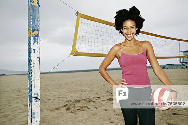 Mixed race woman holding volleyball on beach