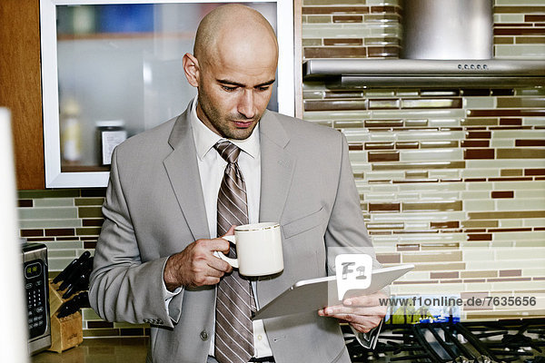 Hispanic businessman using tablet computer in kitchen