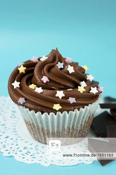 Ein Cupcake mit Schokocreme und Zuckersternchen im Papierförmchen auf Tortenpapier  Schokoladenstücke