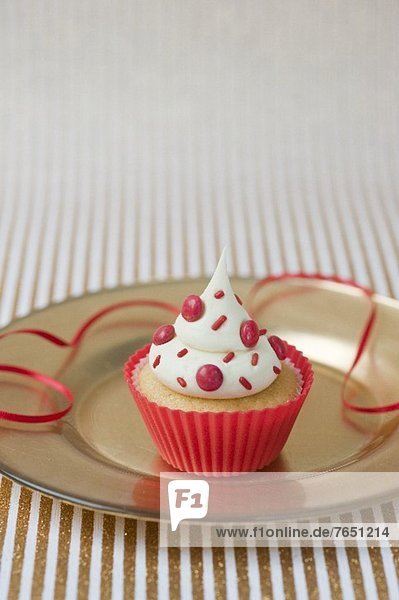 Vanille-Cupcake mit roten Schokolinsen im roten Plastikförmchen für eine Party