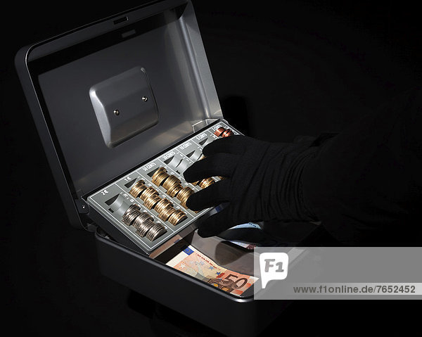 Hand wearing a black glove reaching for money  euro coins and euro notes  in a cash box