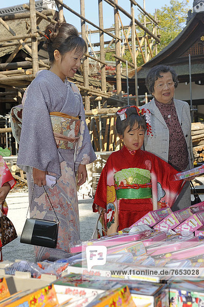 Shichi-go-san  Seven-Five-Three festival  a girl in a kimono with hair jewellery  her mother also in a kimono and her grandmother are selecting a gift  Kamigamo Jinja Shrine  Kyoto  Japan  East Asia  Asia