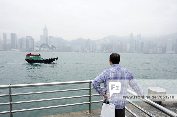 Man standing at the waterfront in Tsim Sha Tsui  Kowloon  looking at the Victoria Harbour and Hong Kong Island  Hong Kong  China  Asia