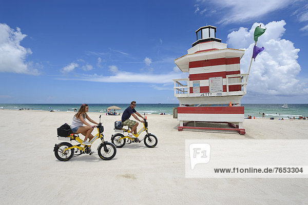 Couple riding electric bicycles  Watchtower  The Jetty  Miami Rescue Tower  South Beach  Miami  Florida  USA