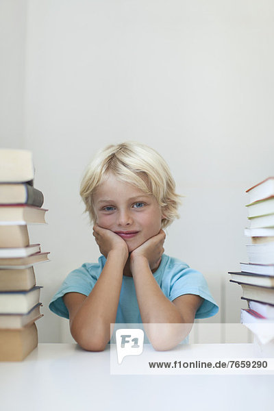 Junge sitzt zwischen hohen Buchstapeln  Porträt