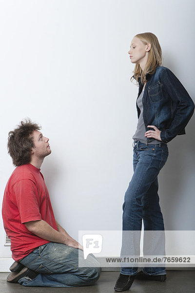 Young man kneeling in front of angry girlfriend