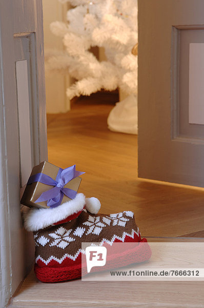 Wollhausschuh mit Norwegermuster und Geschenk steht vor geöffneter Wohnungstür