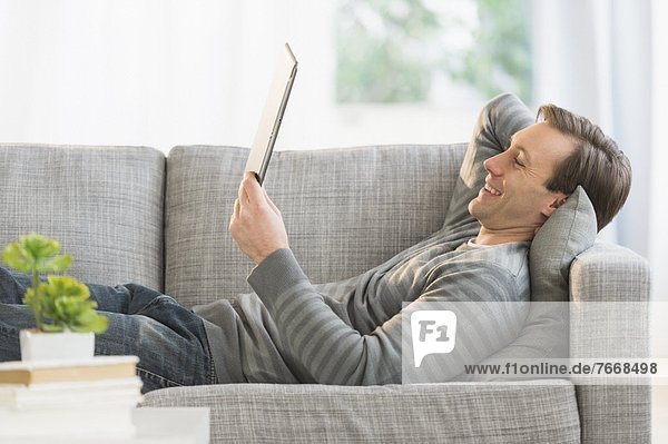 Man lying on sofa watching tablet pc